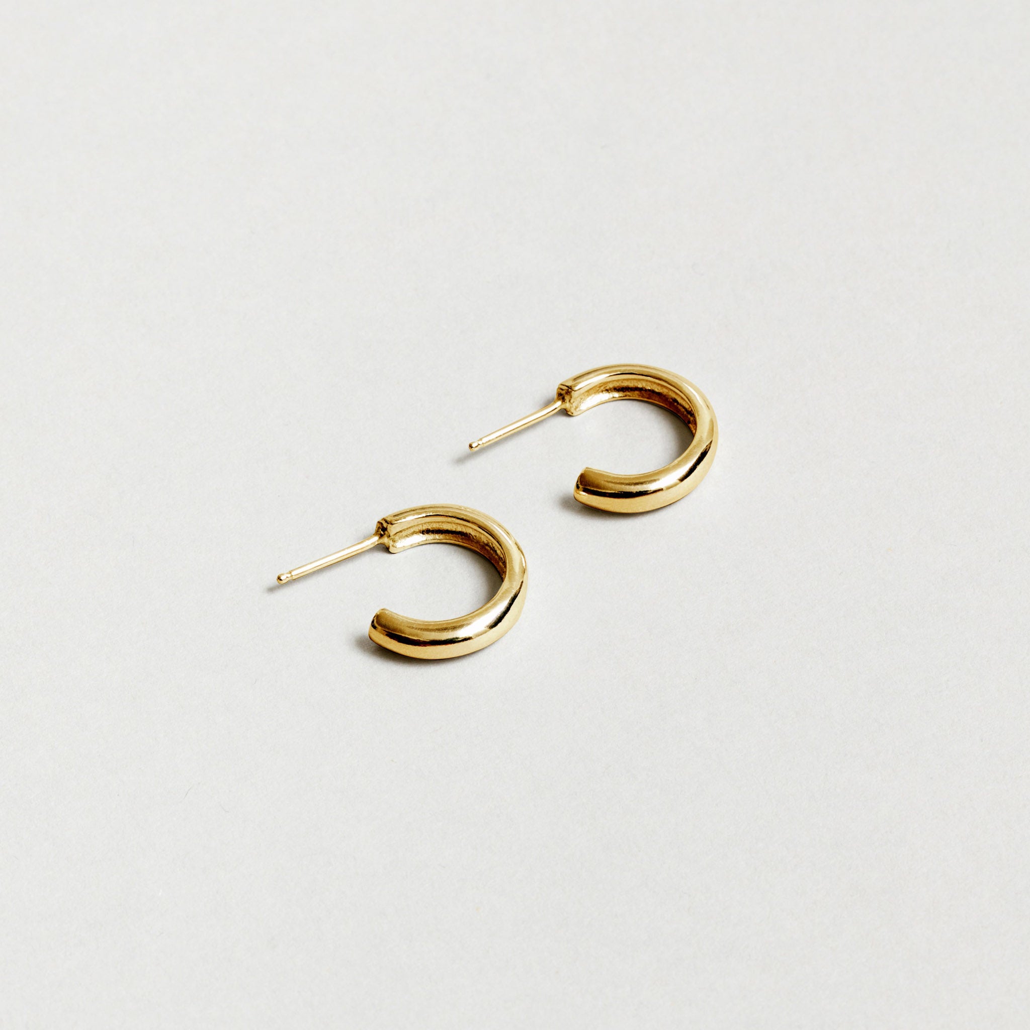Small gold hoop earrings rest against a white background. 