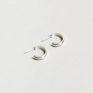 Small sterling silver hoop earrings rest against a white background. 