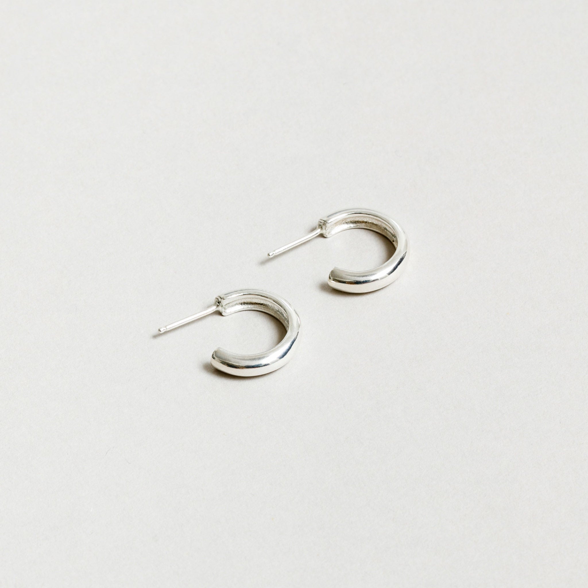 Small sterling silver hoop earrings rest against a white background. 