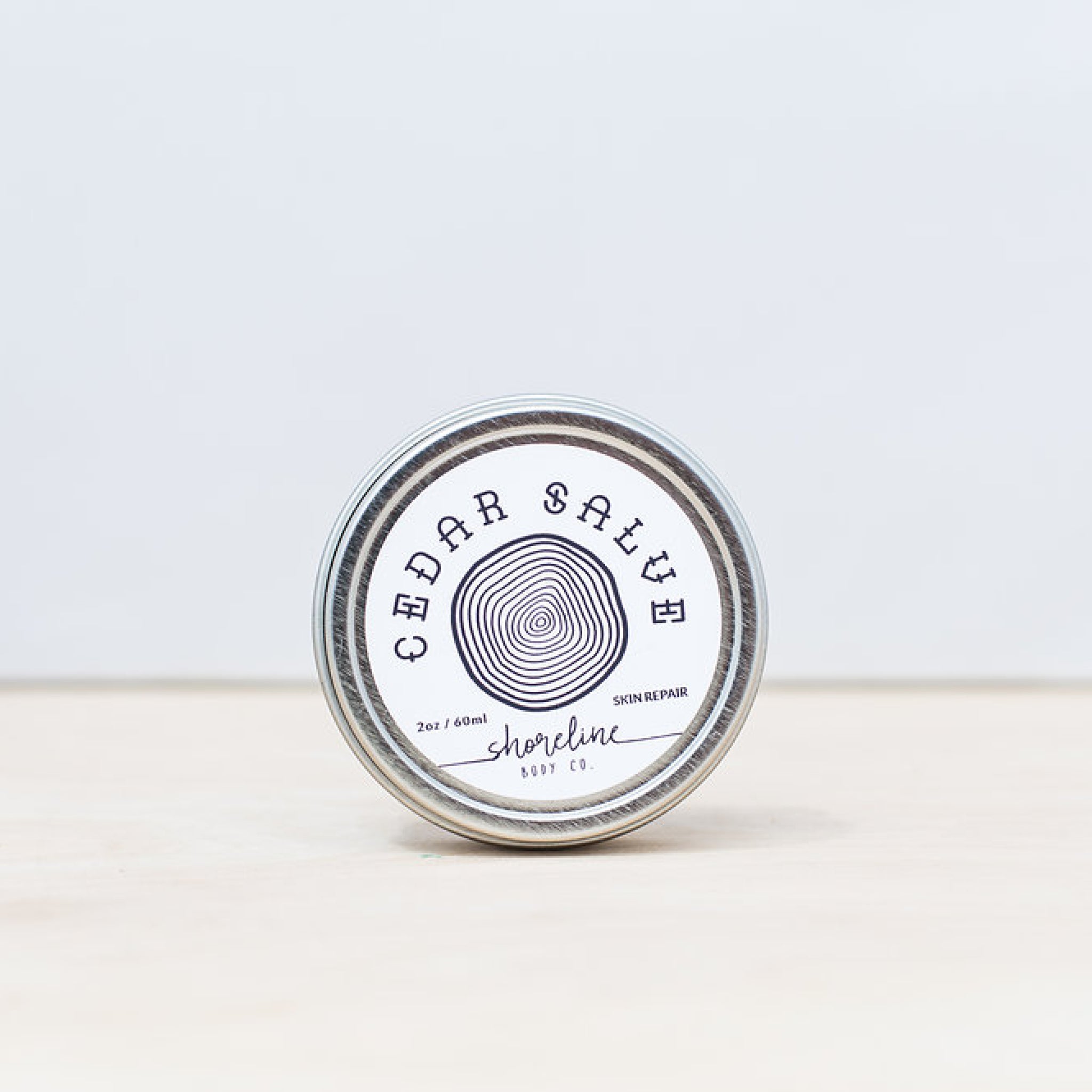 The cedar salve is pictured in it silver tin against a white background. 