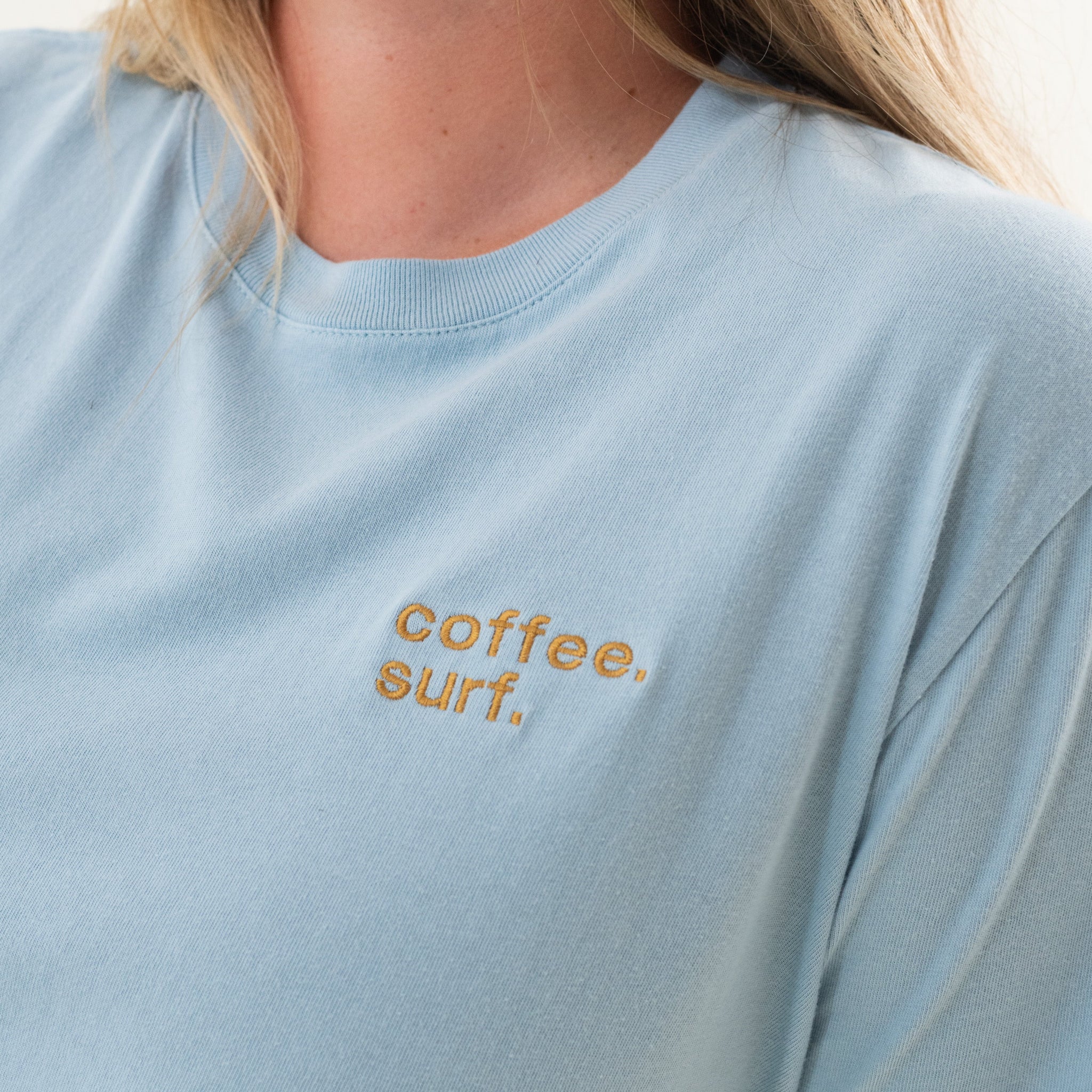 Organic cotton t-shirt in a creamy blue with "coffee. surf." embroidery over the left chest. 