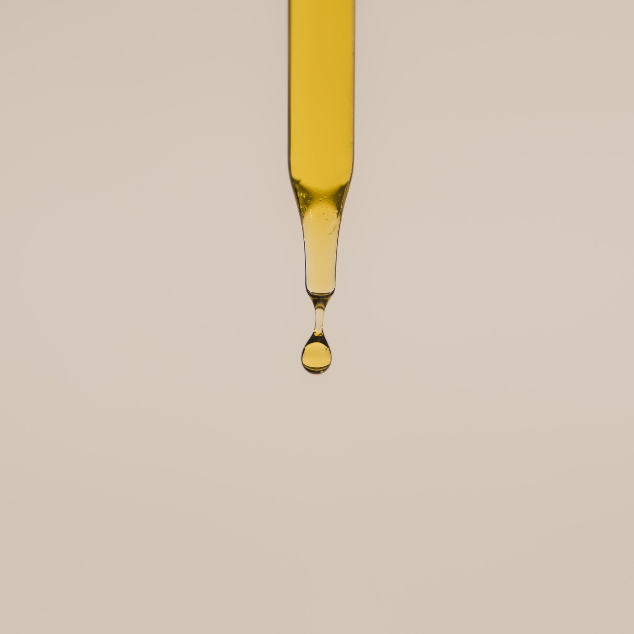 A close up image of the Eternal Serum dropper, dispensing a single drop of golden oil.  
